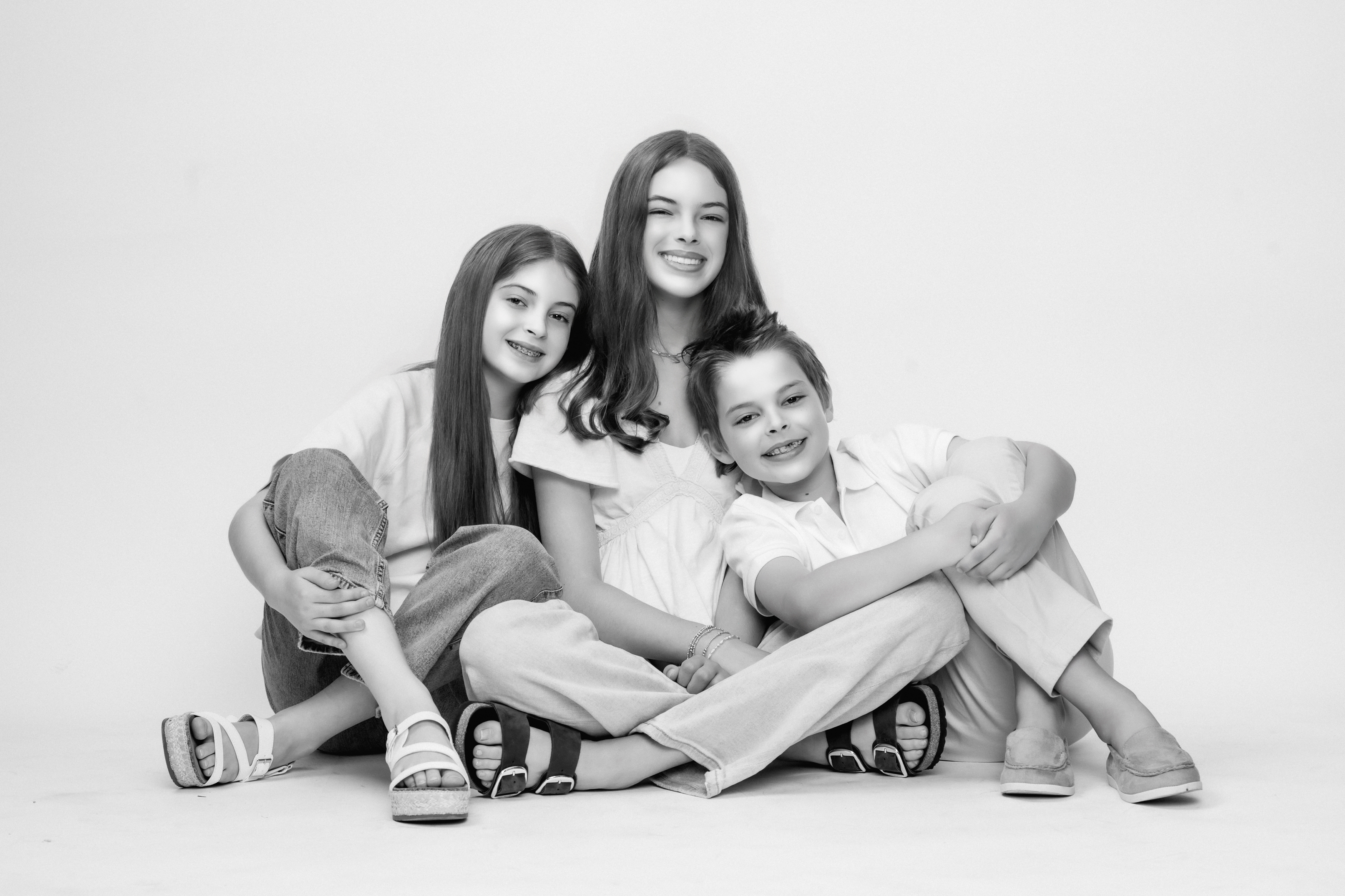 Three siblings sit together in a timeless black-and-white studio family portrait in Nashville, Tennessee, smiling and leaning into one another with genuine sibling connection.