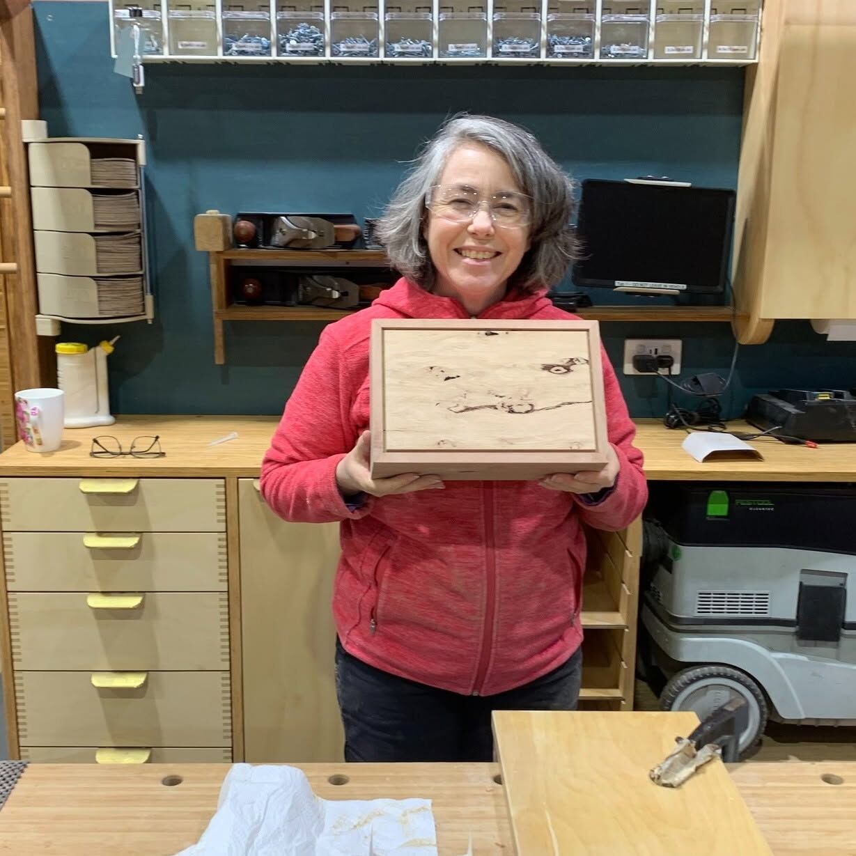 Robyn smiling in the workshop, holding the timber box she made