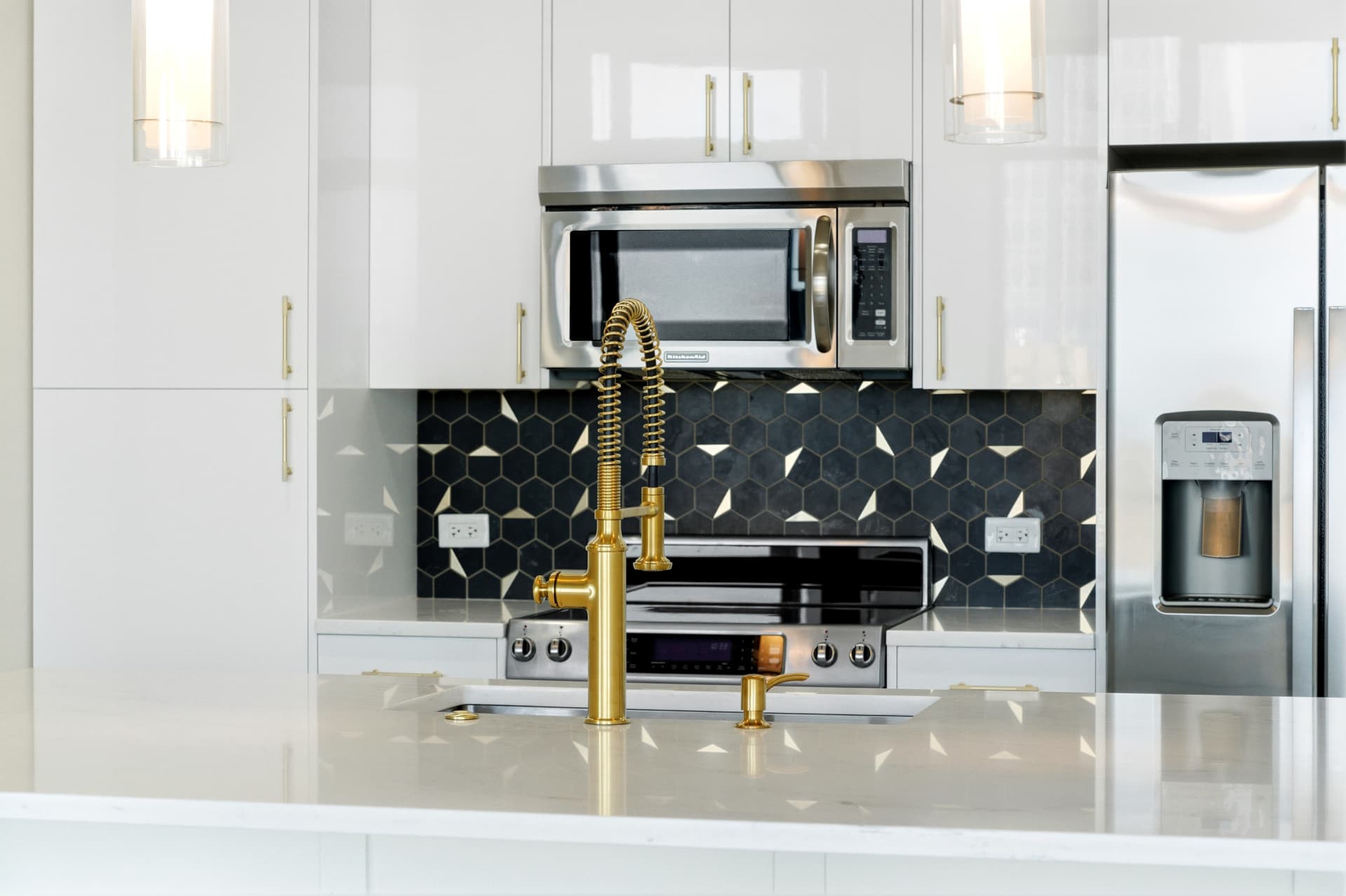 Full kitchen with quartz island, gold pre-rinse faucet, glass pendants and floor-to-ceiling white gloss cabinetry