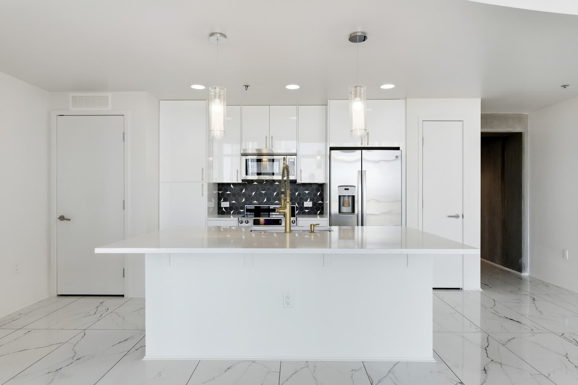 High-gloss white flat-panel kitchen with quartz island, charcoal hexagonal backsplash, gold hardware and glass pendant lights