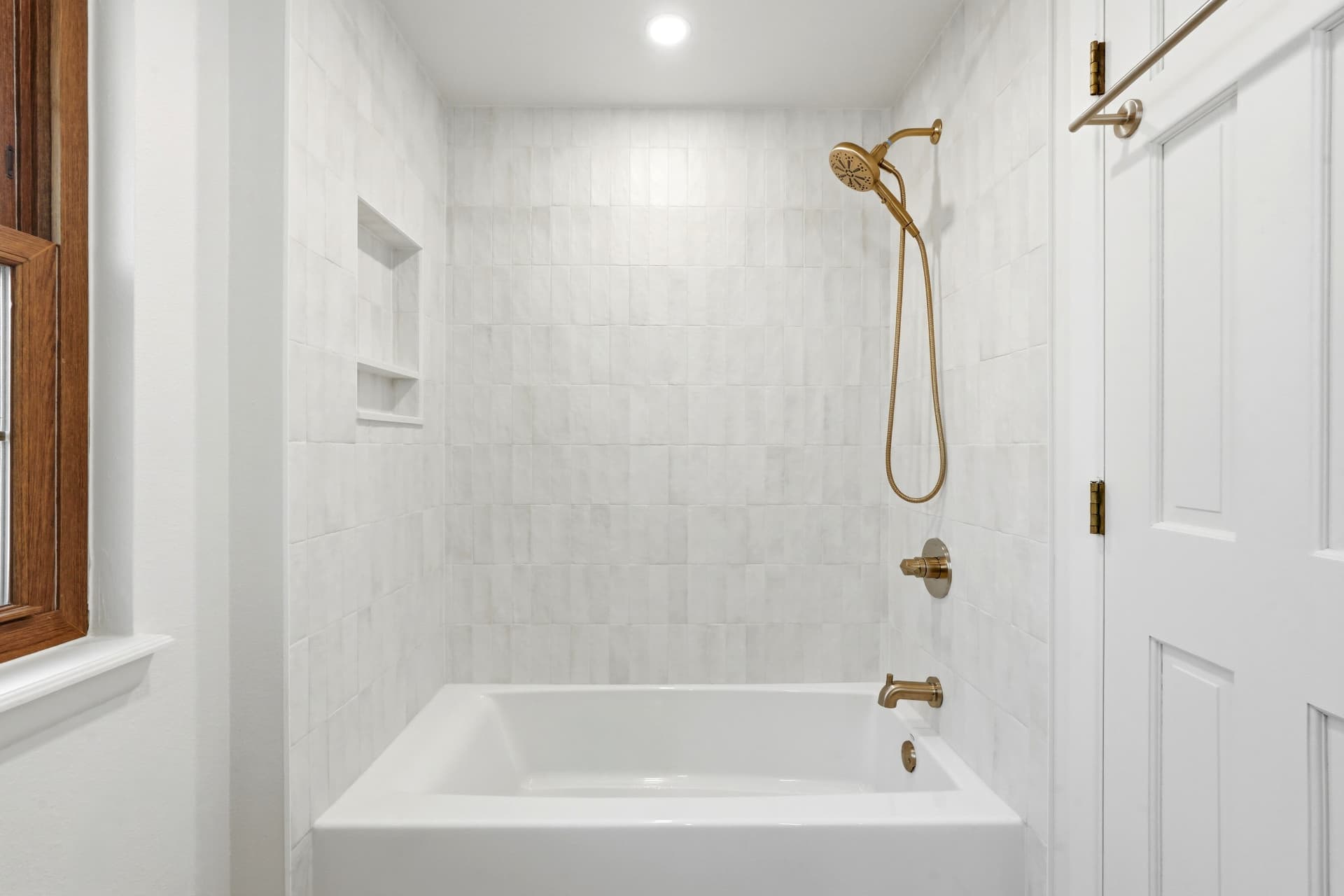 Tub and shower surround in white vertical tile with brushed gold fixtures and recessed niches