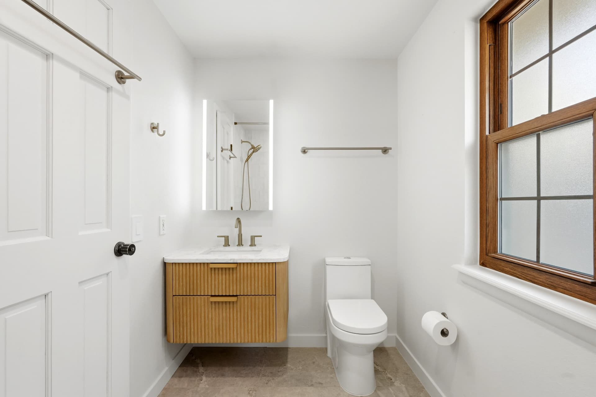 Guest bath with floating fluted oak vanity, marble top and backlit mirror