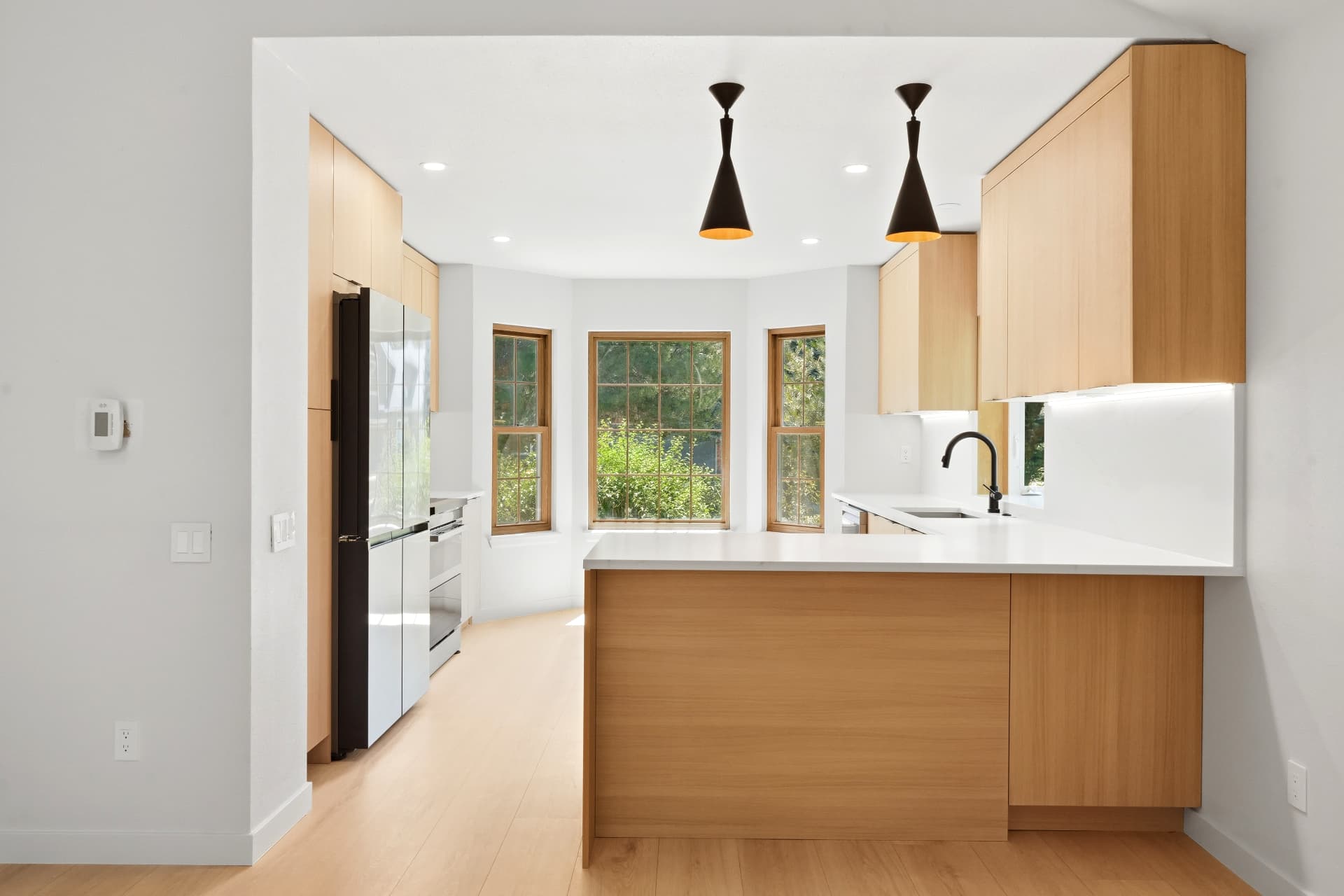 White oak kitchen with quartz peninsula, black cone pendants and bay window