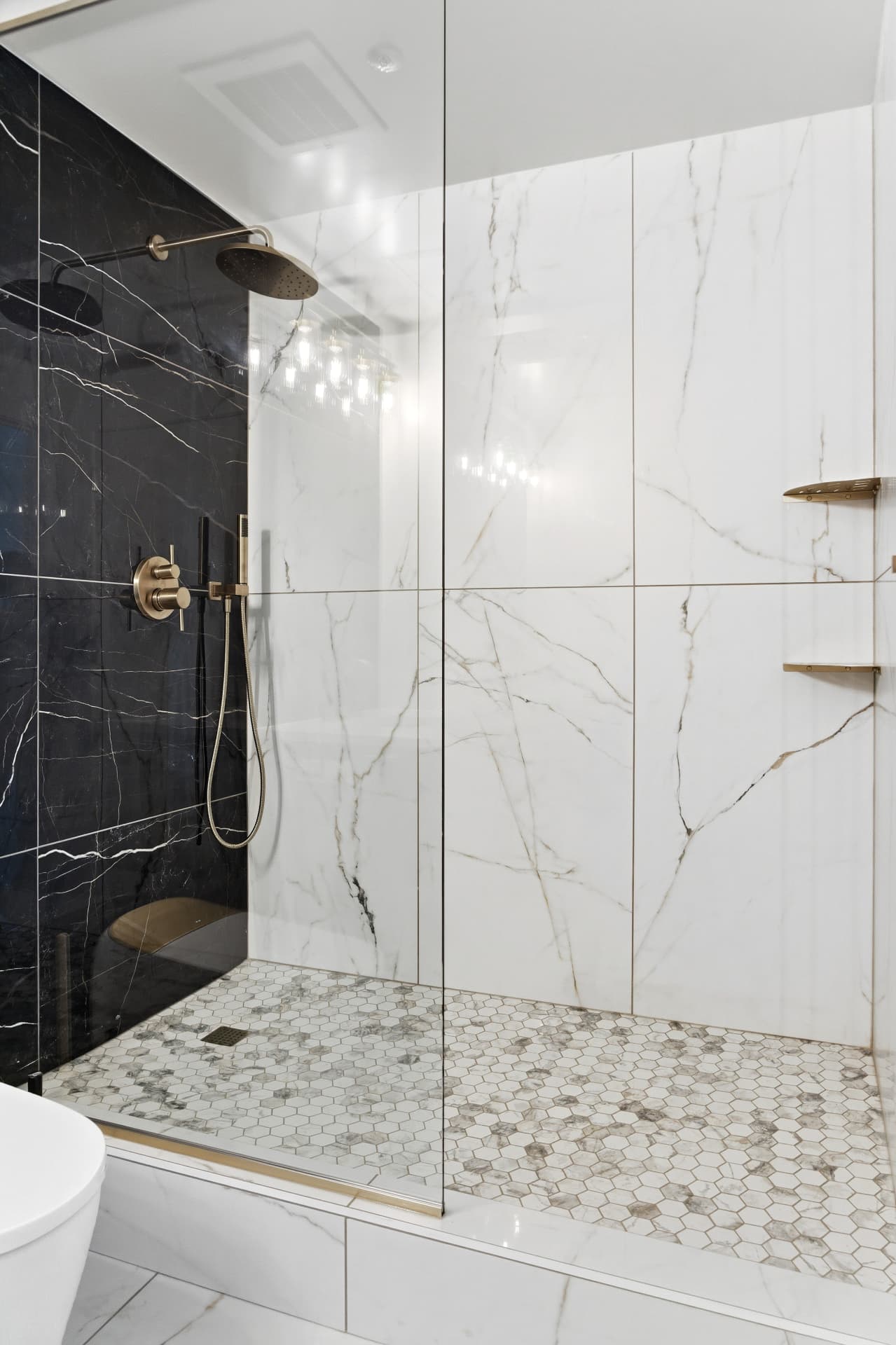 Walk-in shower with frameless glass, hexagonal marble floor mosaic, gold rain head and contrasting black-and-white marble walls