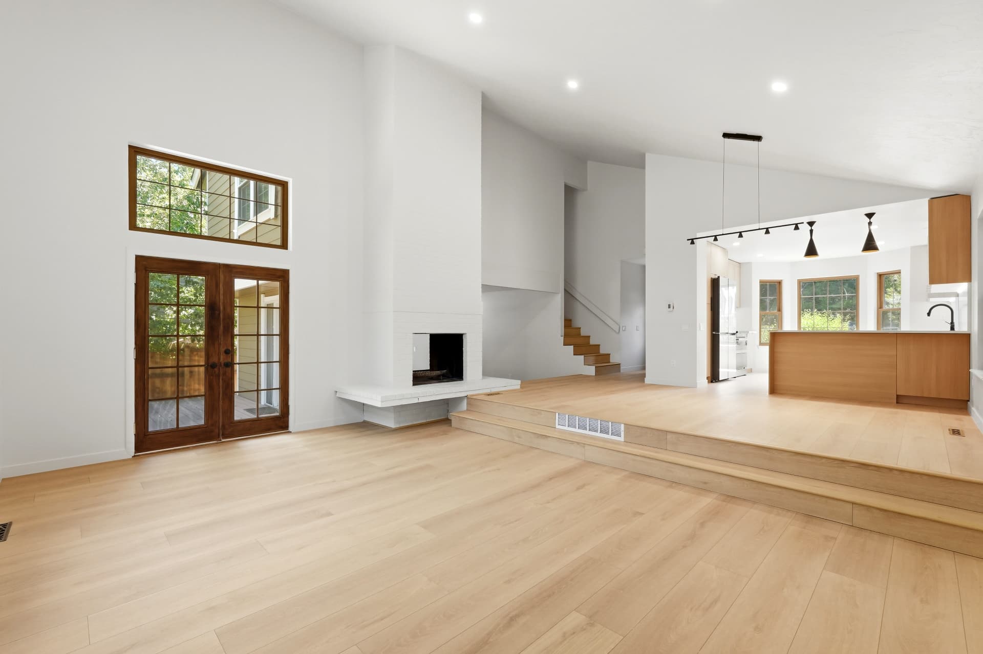 Open-concept great room with white brick fireplace and raised white oak floors