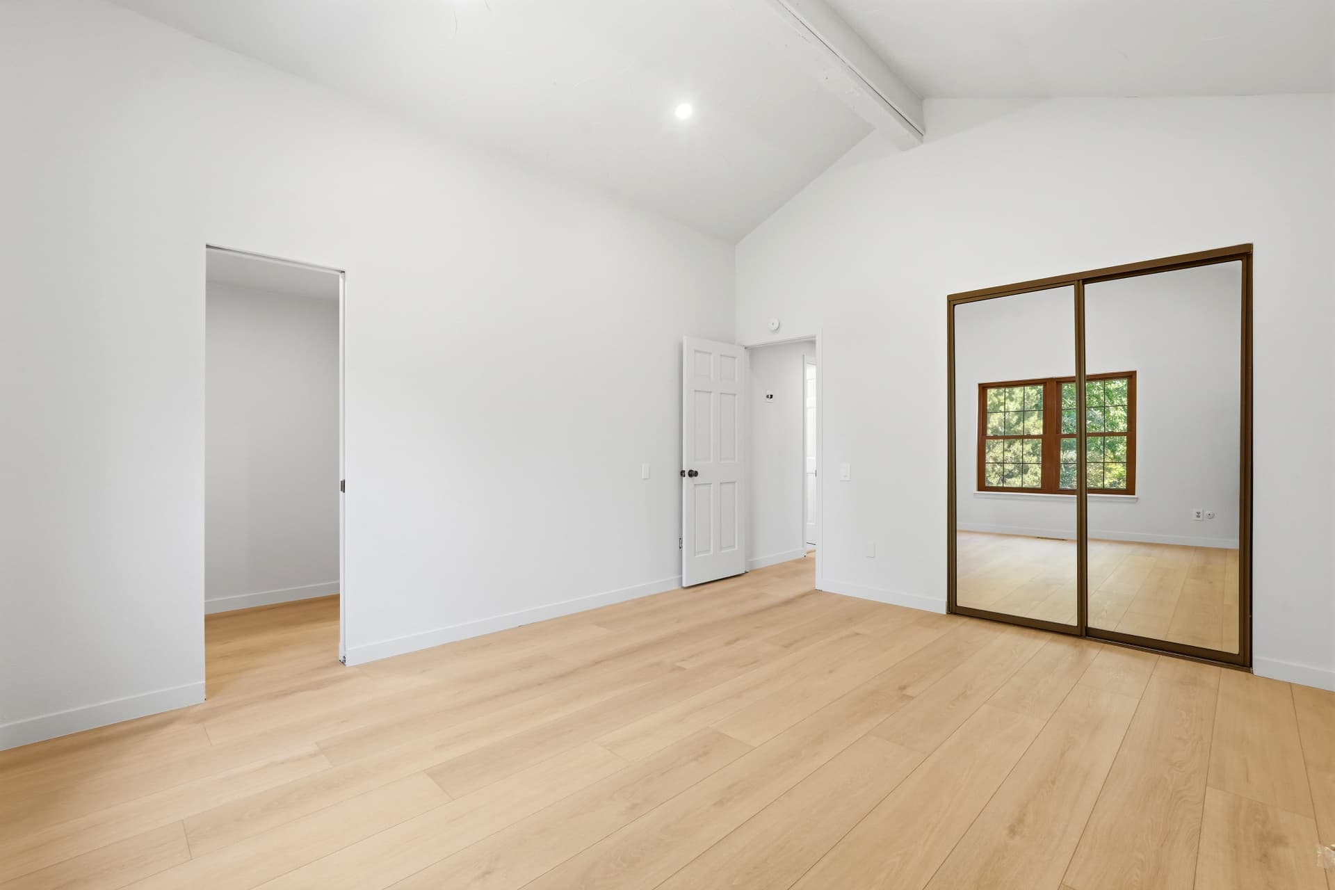 Vaulted primary bedroom with white oak flooring and mirrored closet doors