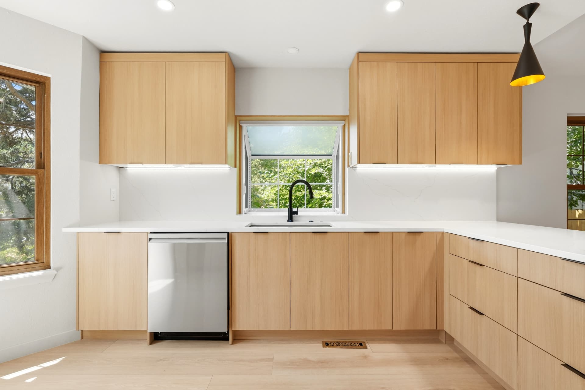 L-shaped light oak kitchen with garden window, quartz backsplash and stainless dishwasher