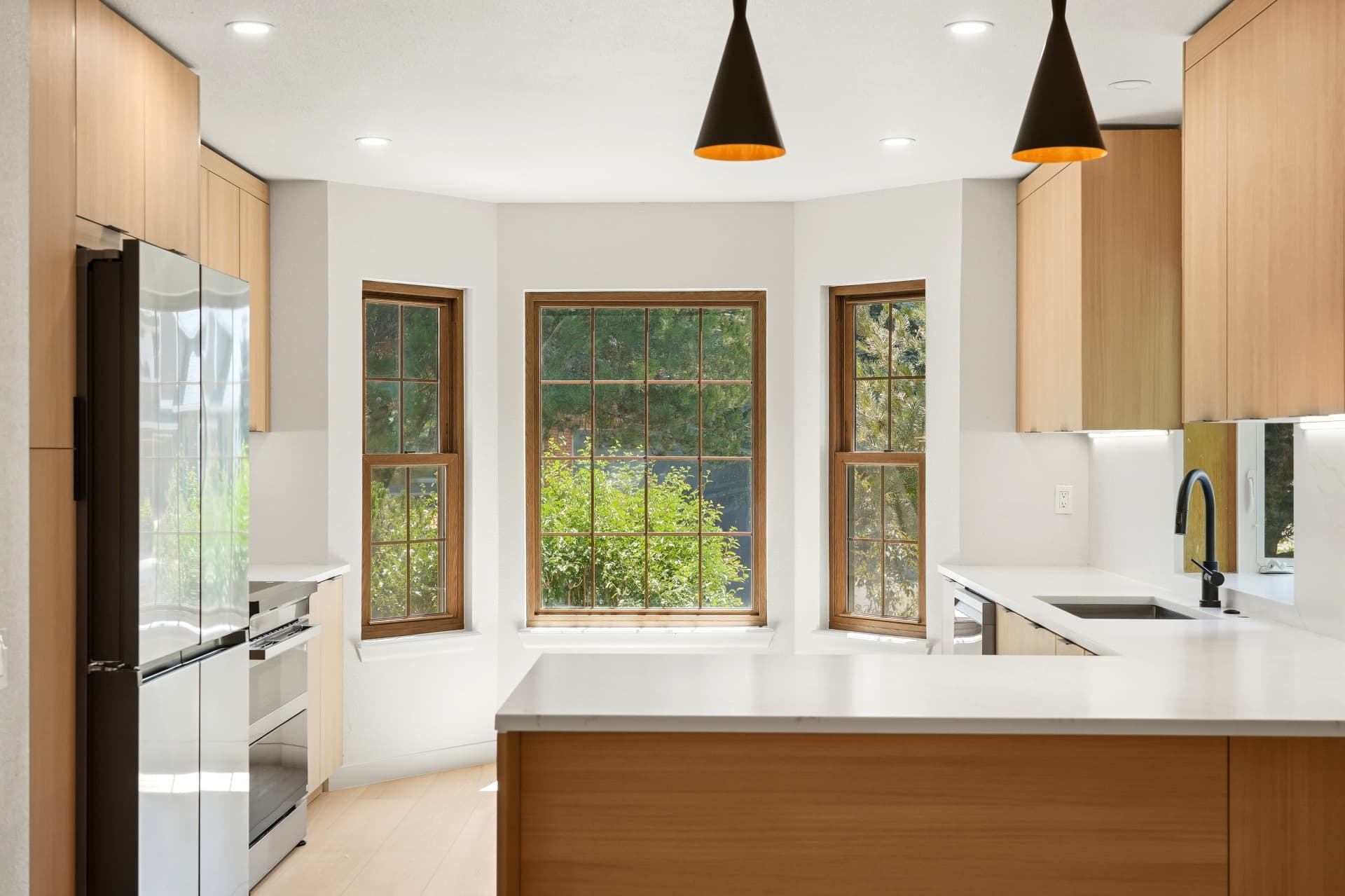 Quartz peninsula kitchen with matte black faucet and bay window seating