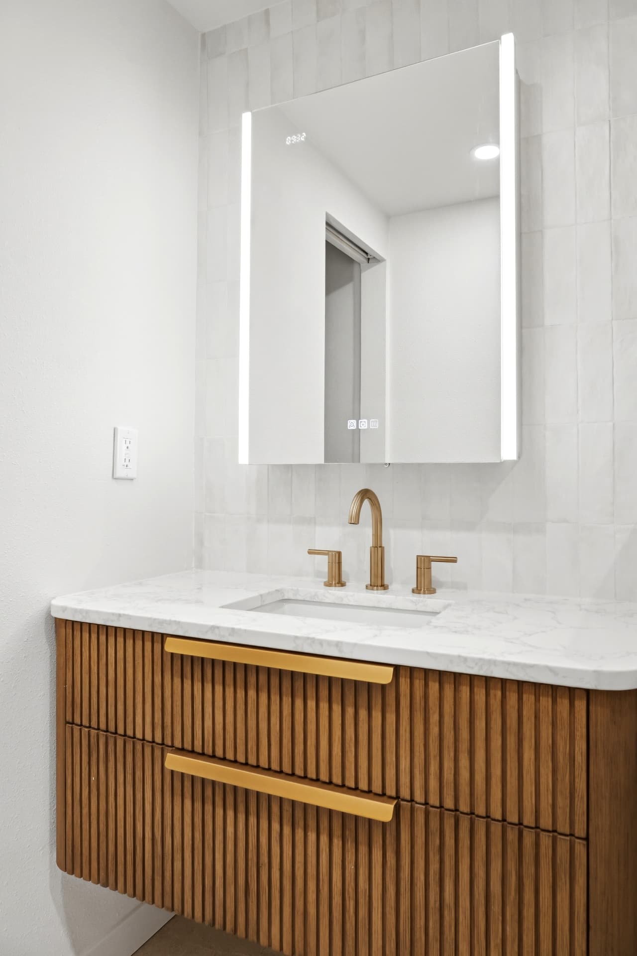 Floating fluted oak vanity with marble countertop and backlit LED mirror