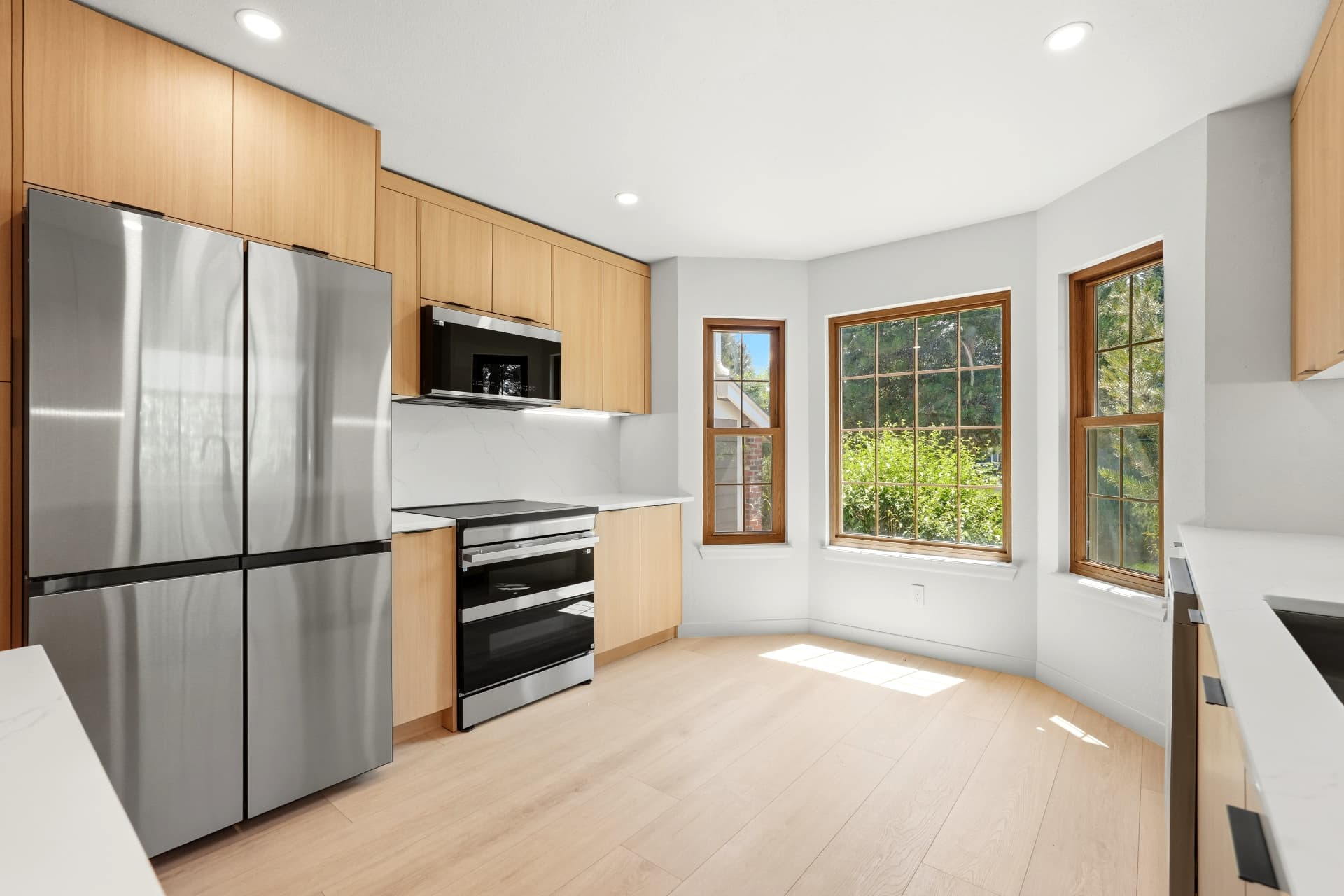 White oak kitchen with slab quartz backsplash, double oven range and bay windows