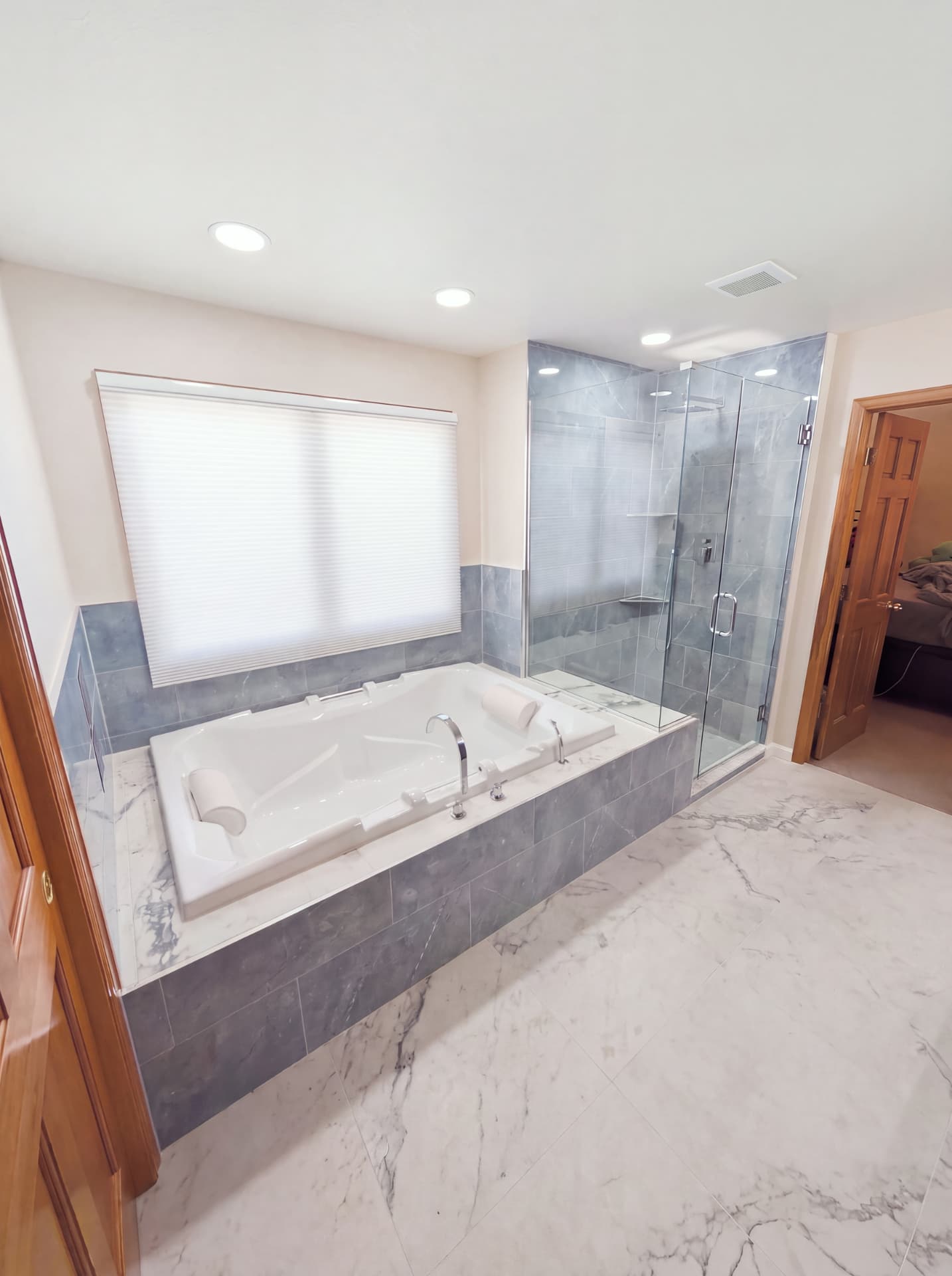 Full view of a bright master bathroom with marble floor, soaking tub and glass shower enclosure