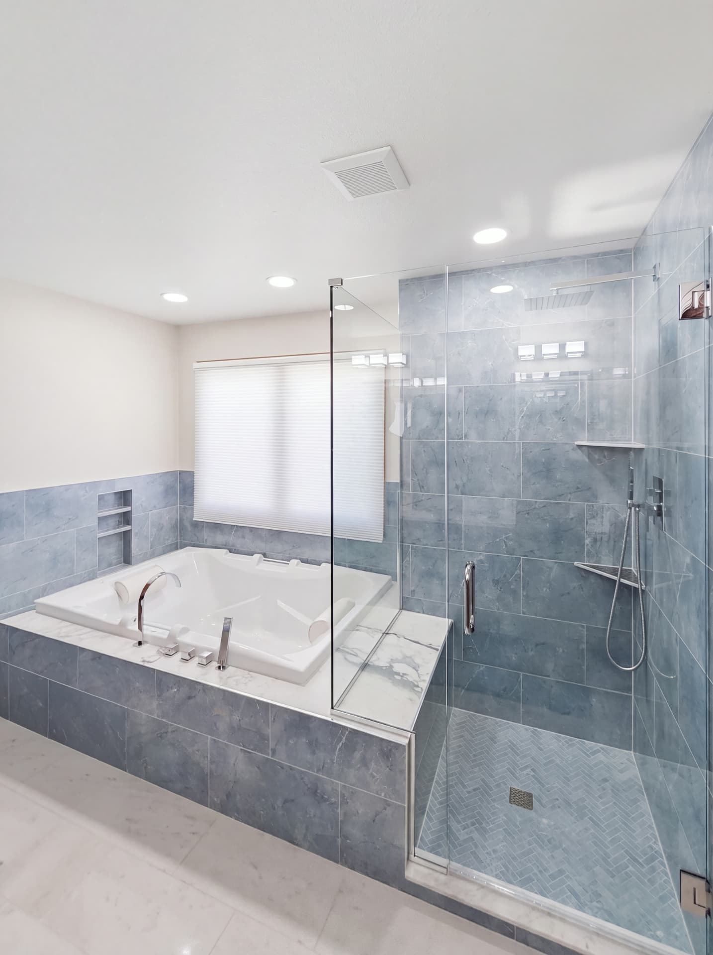 Soaking tub with marble deck and blue-grey tile wainscoting beside a walk-in shower