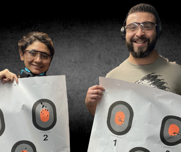 2 smiling students holding their targets at the gun range