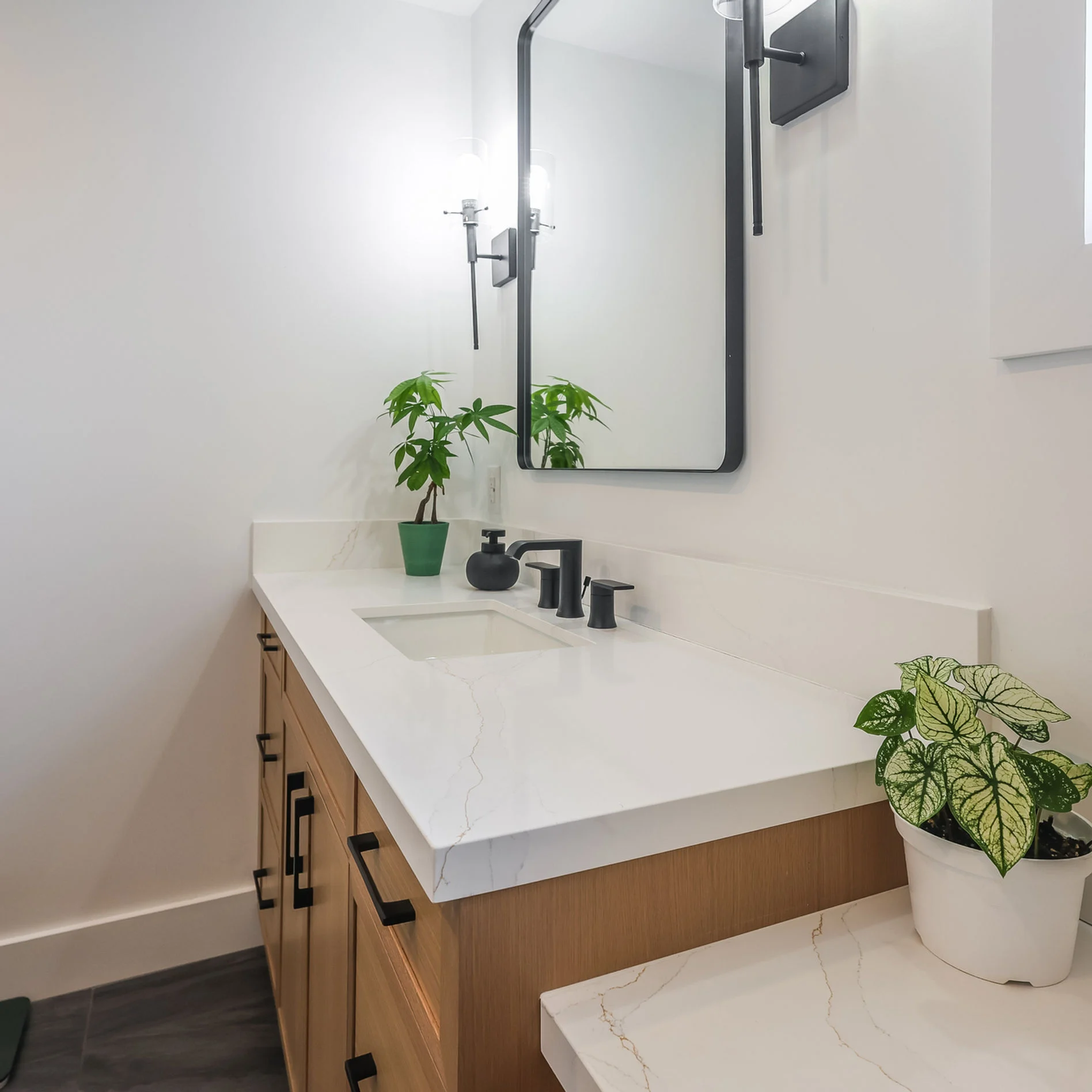 Modern kitchen with white cabinets, a wooden finish oven, and a sleek black faucet over a white countertop. Bright, clean setting.