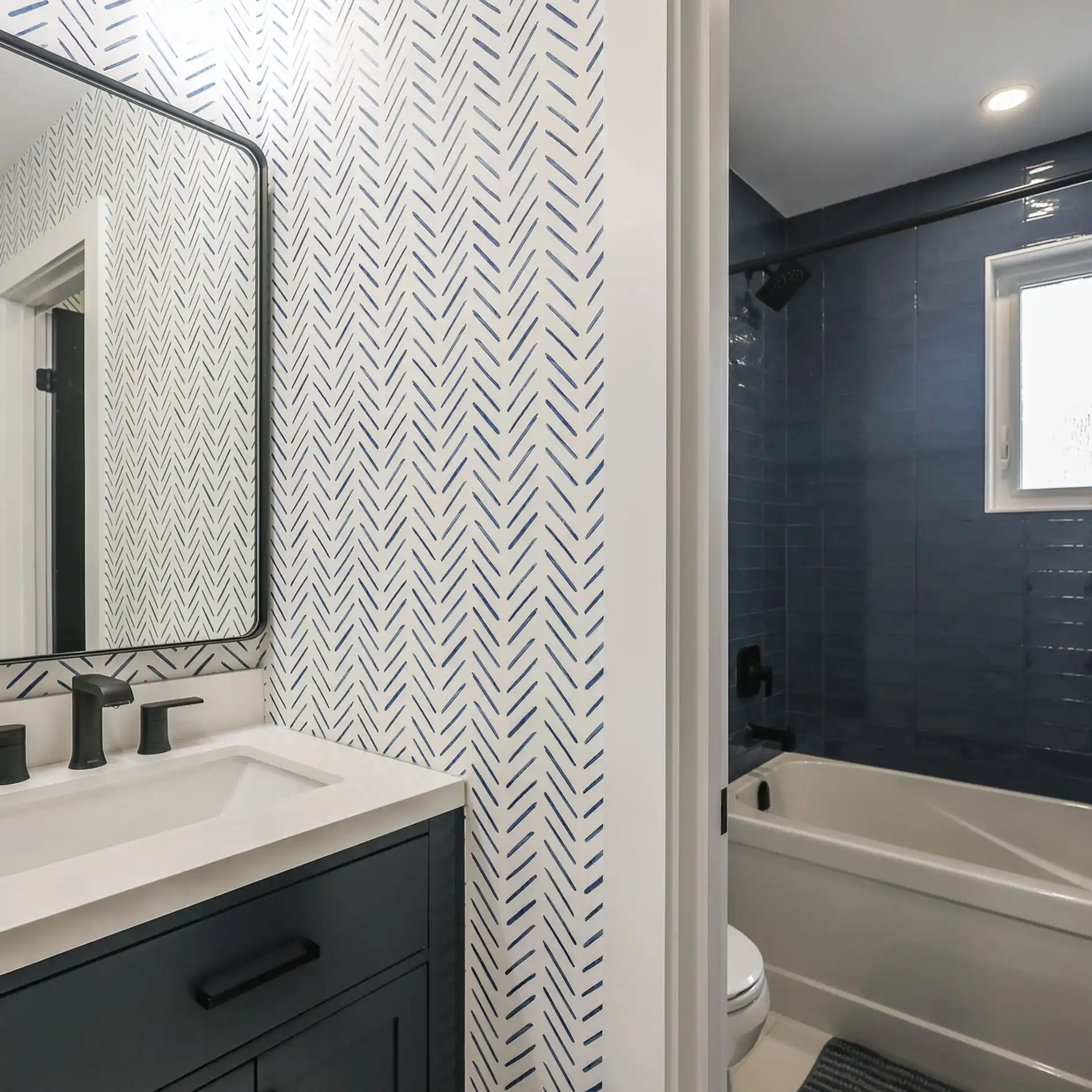 Modern bathroom with a large mirror, dual sinks on a white marble counter, wood cabinets, glass-enclosed shower, and gray-green walls.