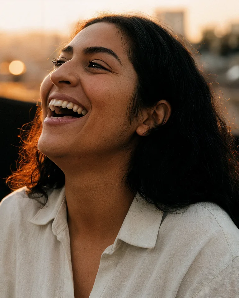 A woman laughs on a rooftop at golden hour.