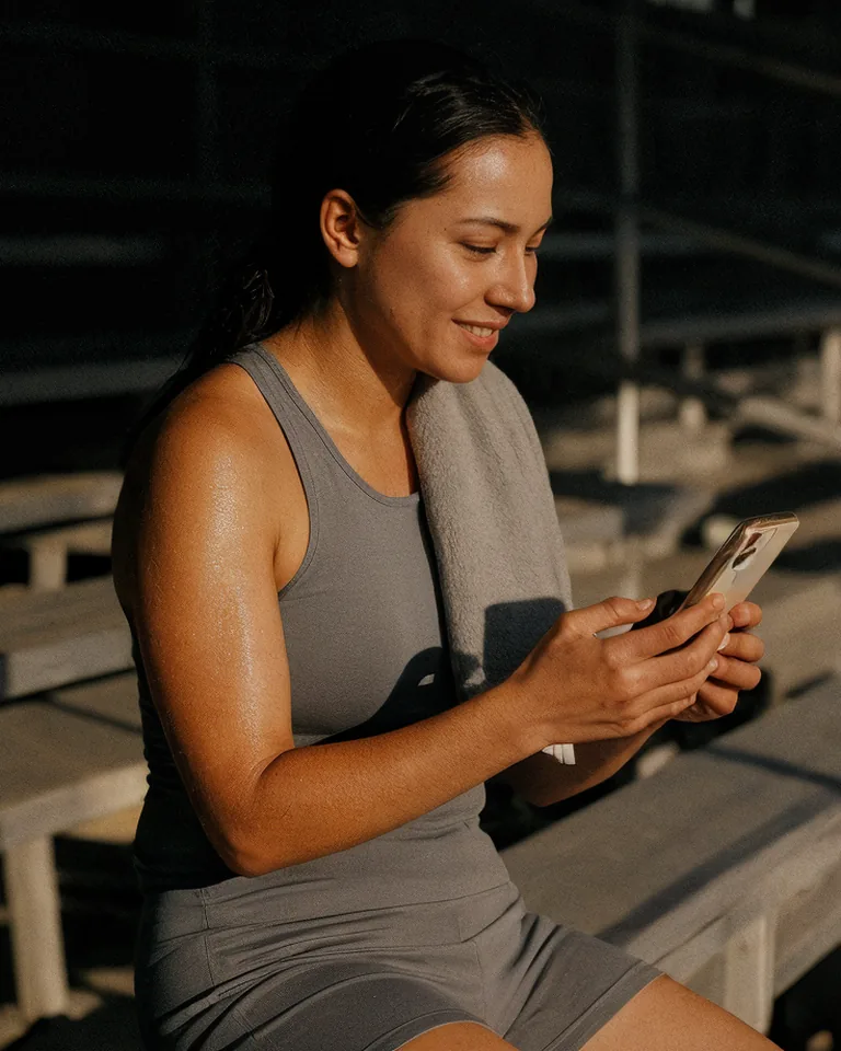 A woman checks her phone on the bleachers after a run.