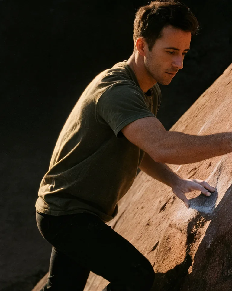 A man climbs a sandstone boulder at golden hour.