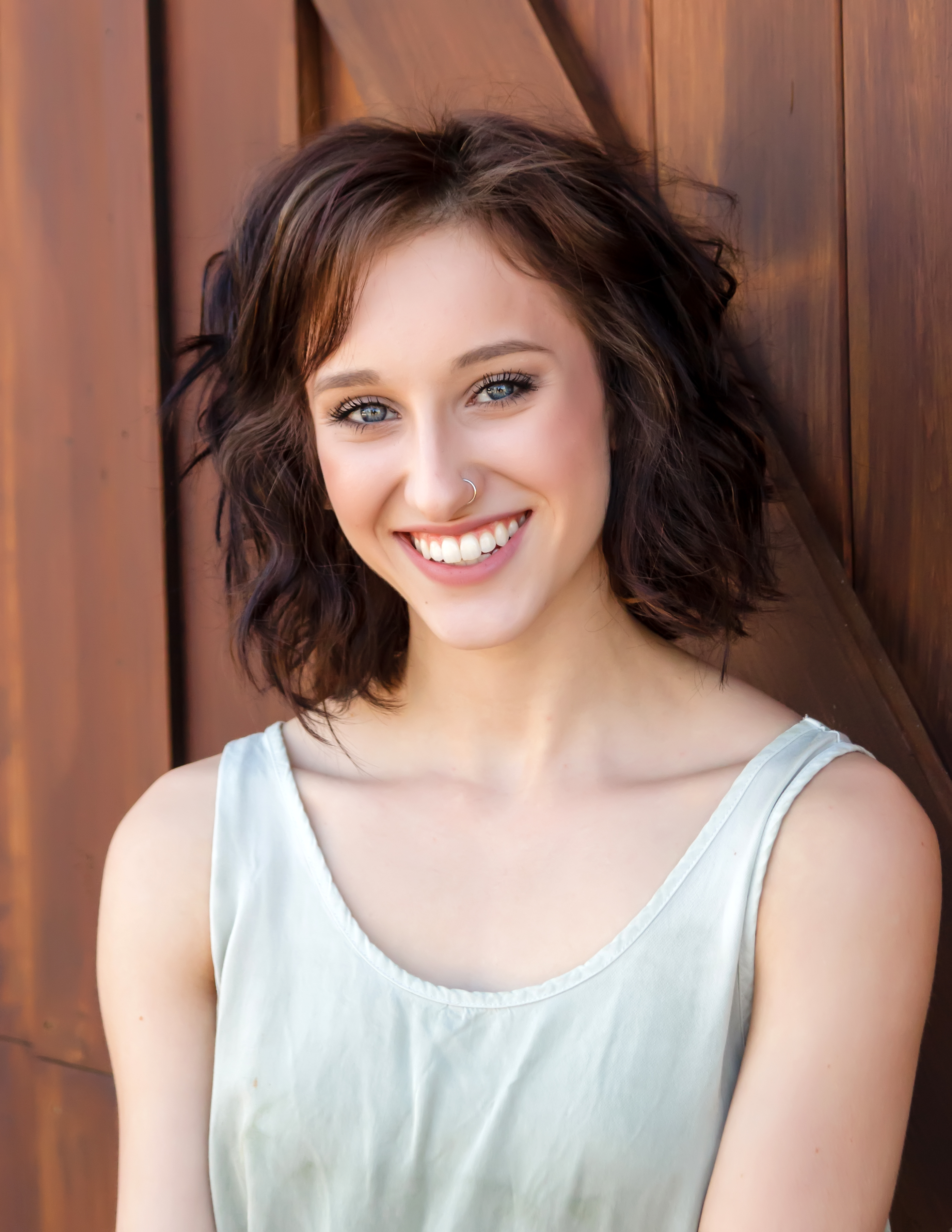 a high school senior girl standing in front of a wooden garage door and smiling at the camera
