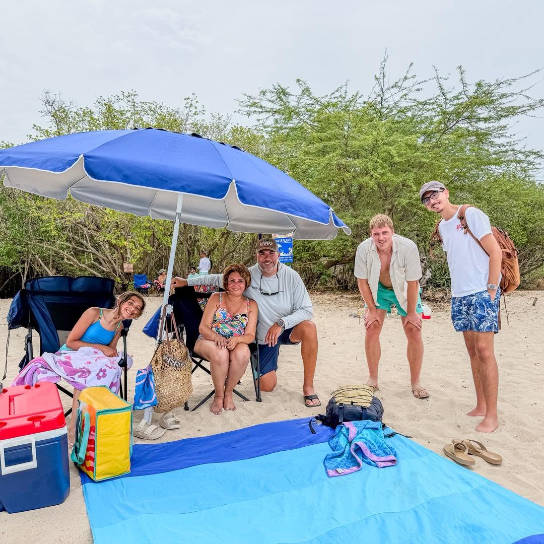 Familia bajo la sombrilla con sillas y nevera en Playa El Combate