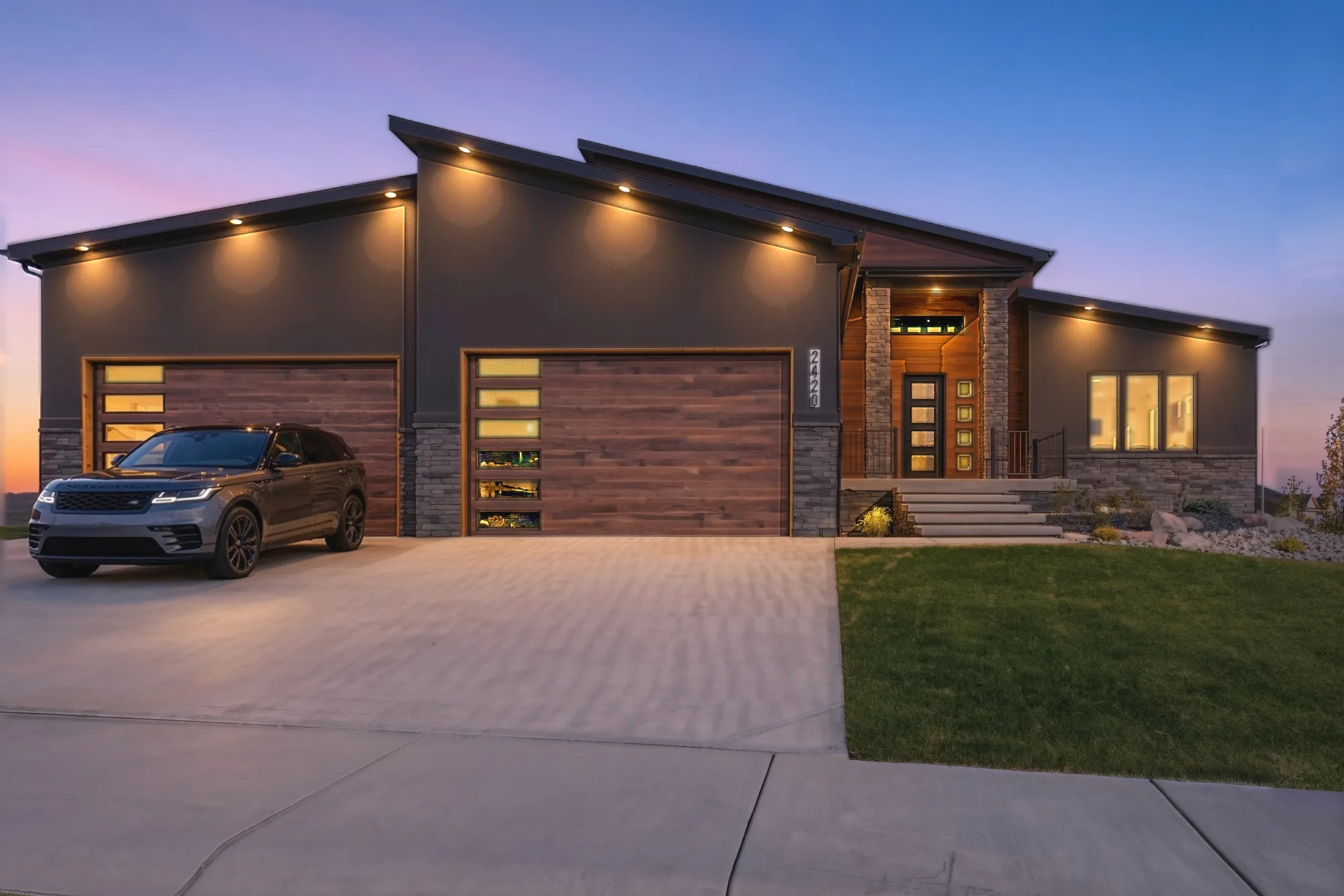 Modern custom home in Casper, WY at dusk with dark siding, stone accents and wood garage doors