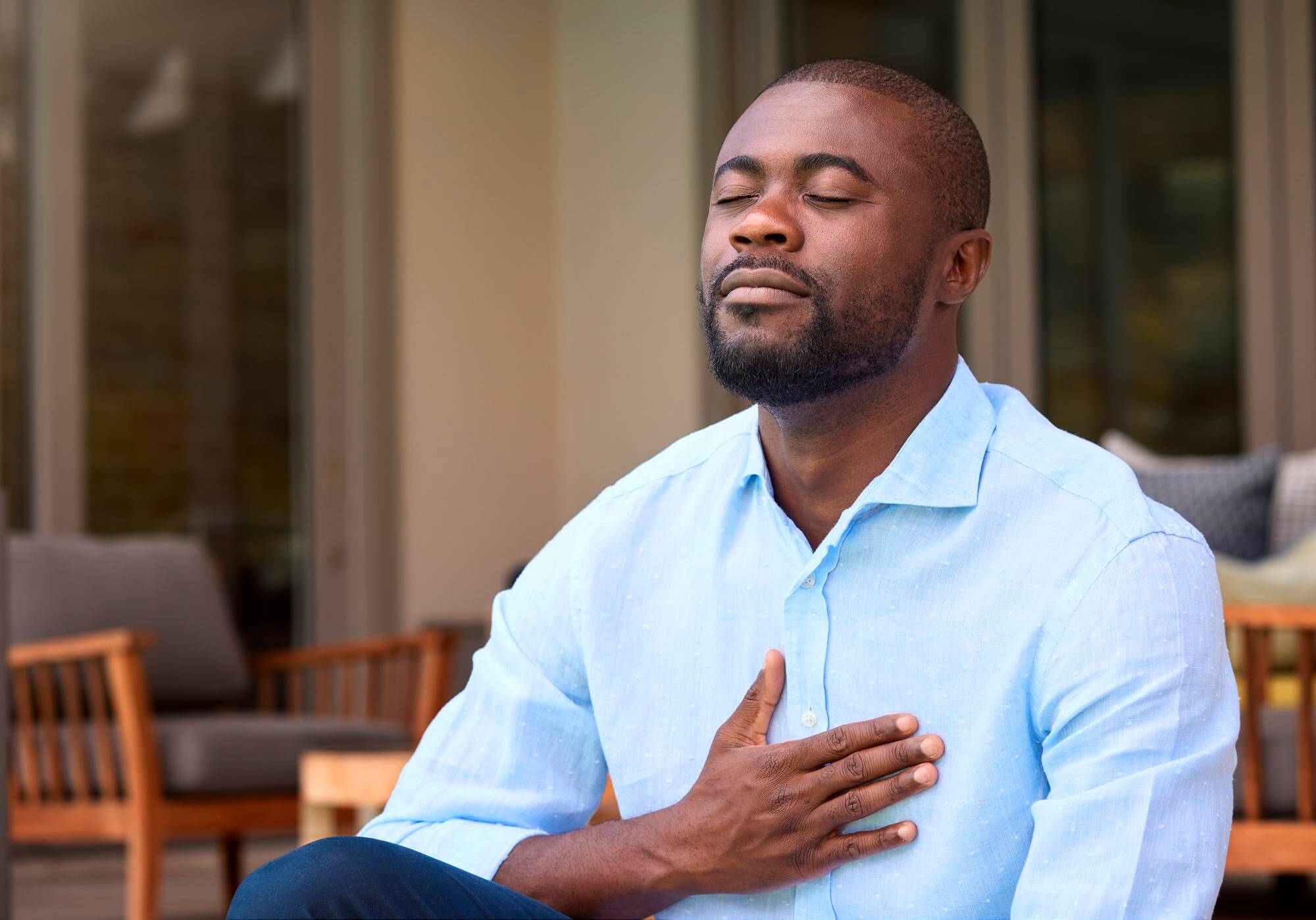 Black man seated in soft light with eyes closed and one hand resting on his chest