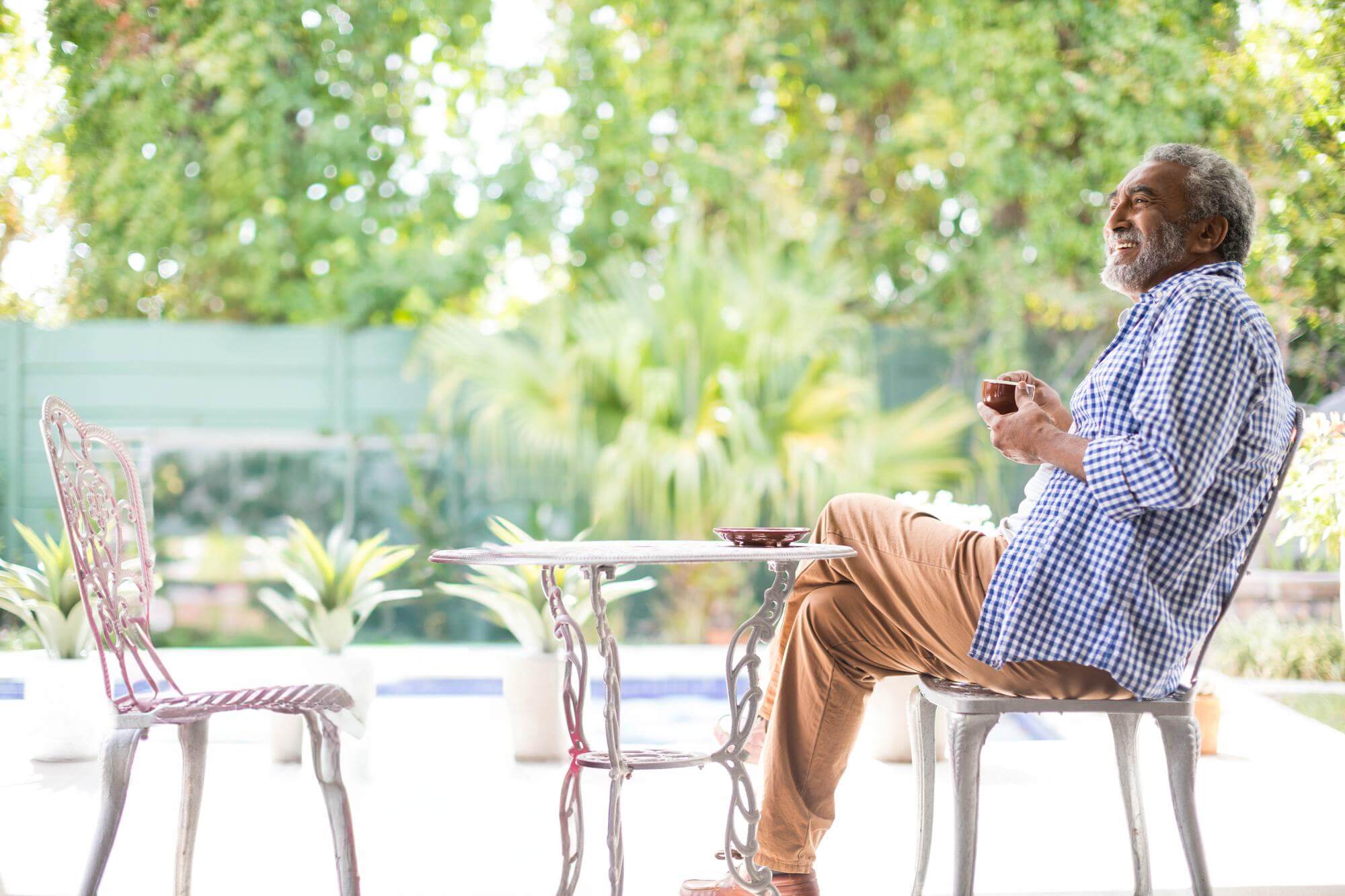 Senior Black man with coffee at a bistro table on a leafy backyard patio
