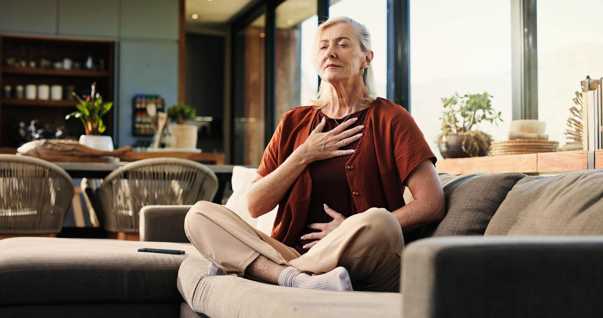 Senior woman on a sofa with one hand on her chest and one on her belly, eyes closed