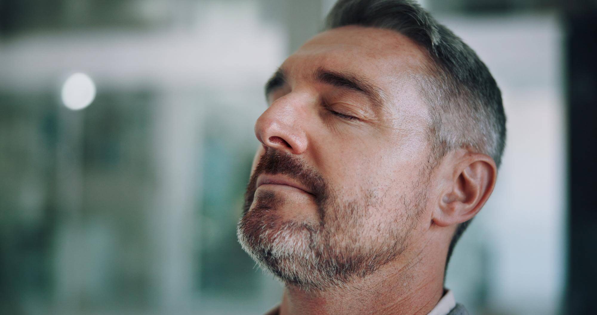 Close-up of a gray-haired man with eyes closed, mid-breath, calm focused expression