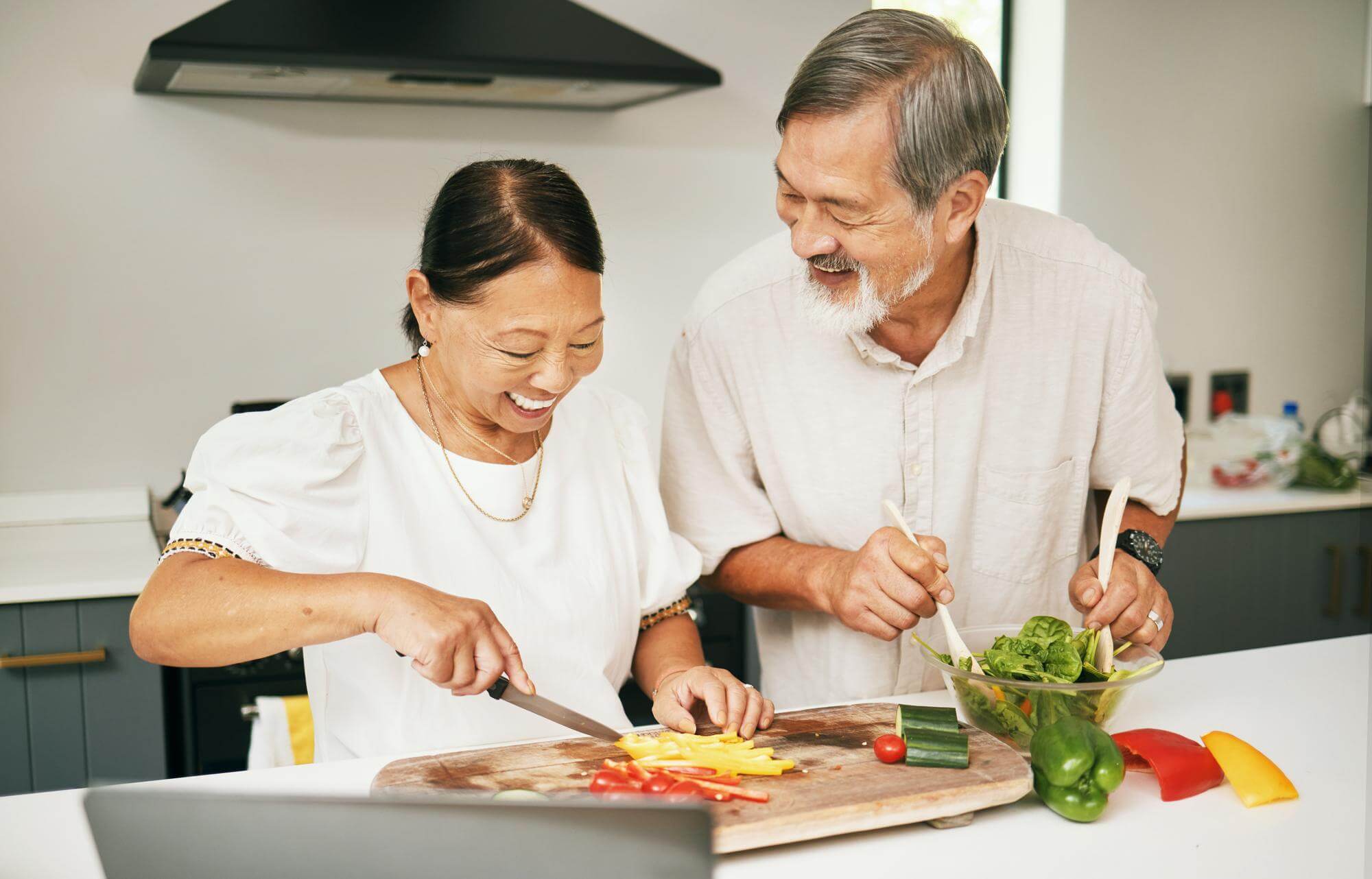Senior Asian couple chopping colorful vegetables together in a bright kitchen