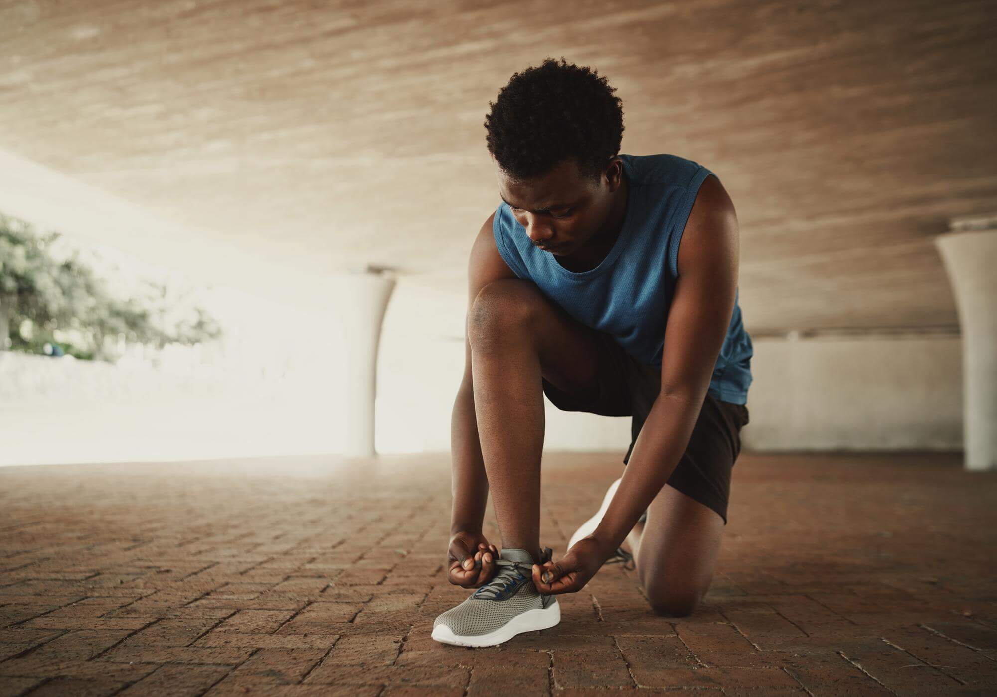 Black man crouching to tie his running shoe in warm early-morning light