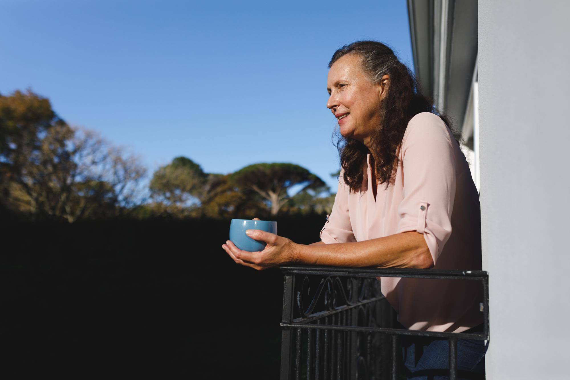 Latina woman holding a mug on a balcony at dusk under a deep blue sky