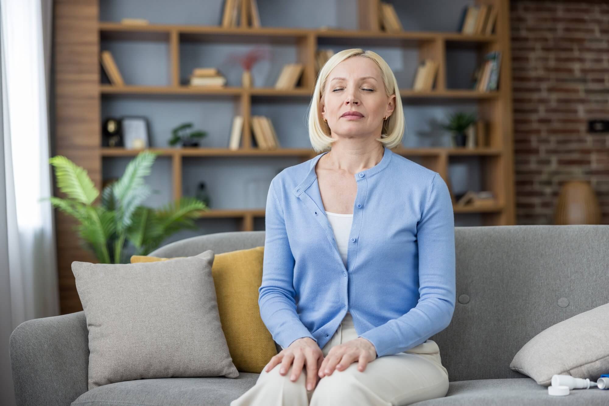 Mature woman seated upright on a sofa, eyes closed, hands resting on her lap