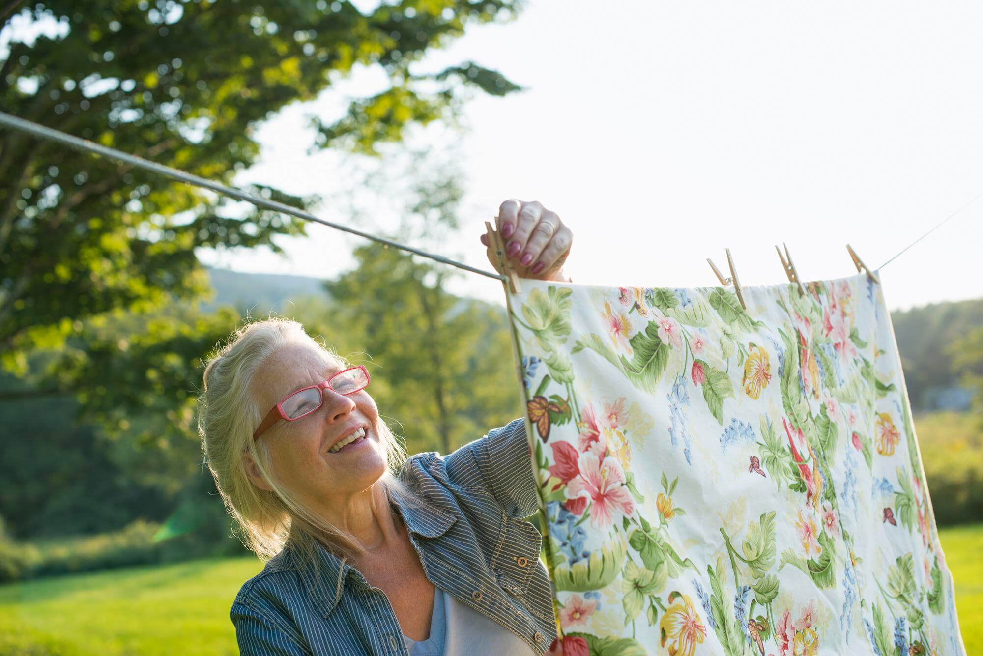 Senior woman pinning a floral sheet to a clothesline in bright summer sunlight