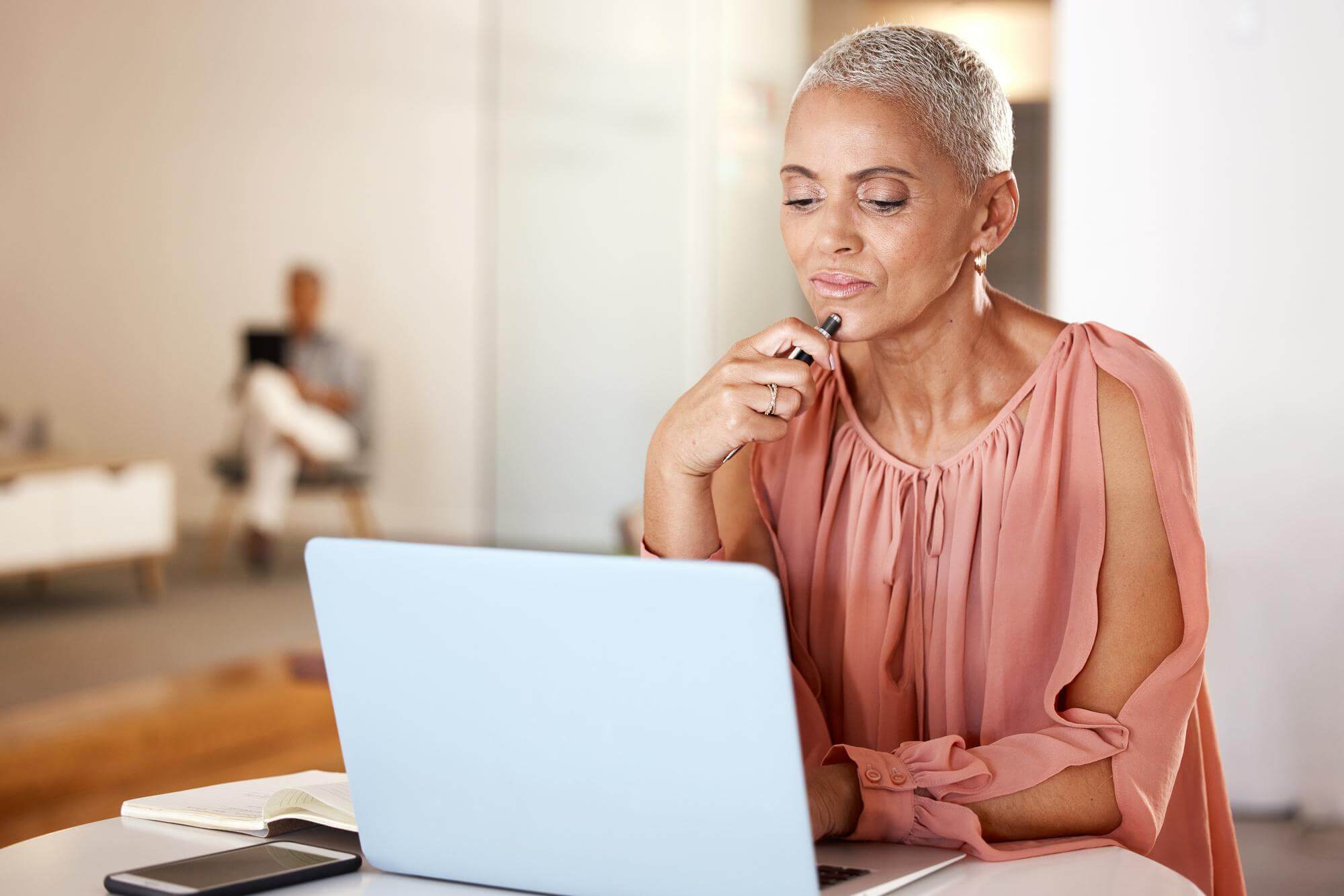 Mature Black woman pausing thoughtfully at a laptop in a bright home office
