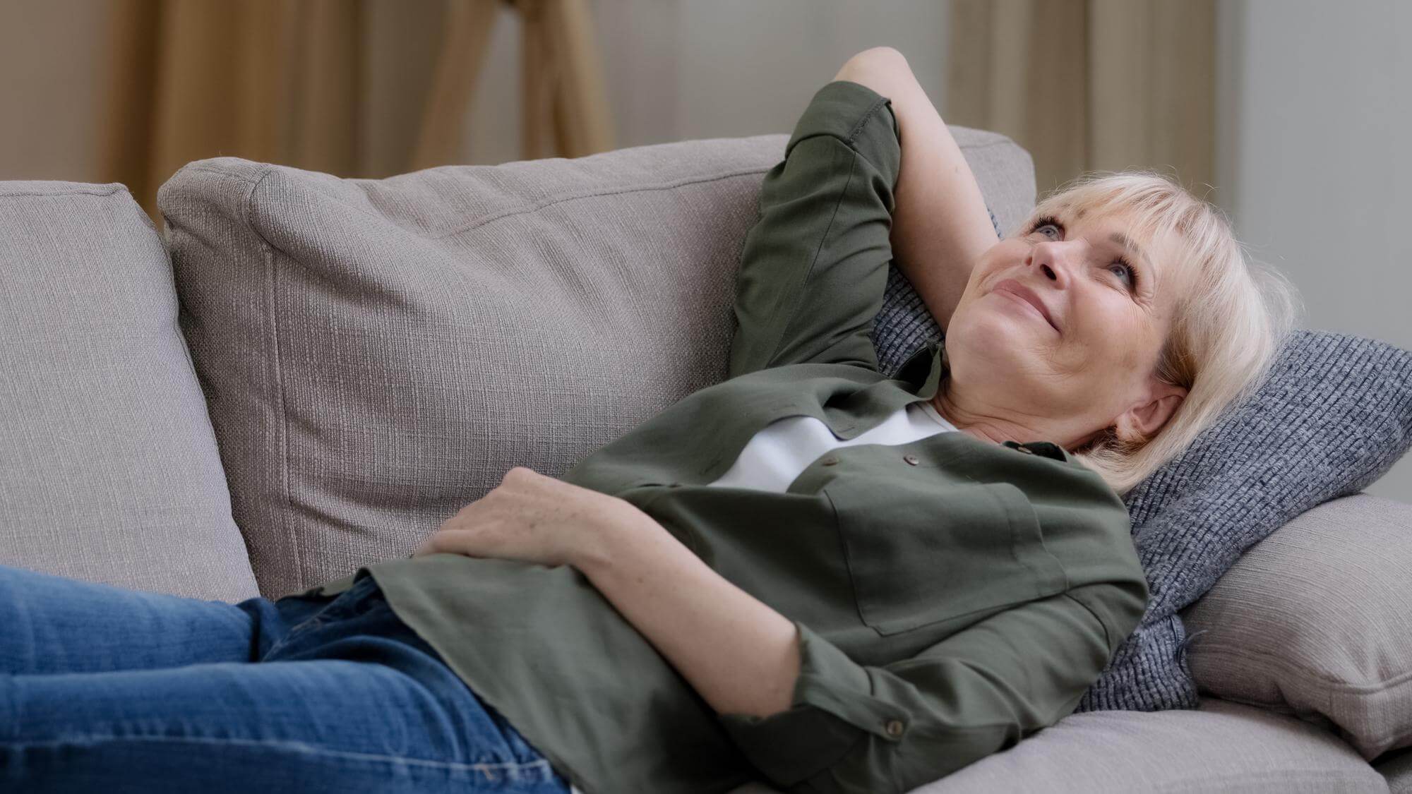 Middle-aged woman lying on a sofa, one hand behind her head and one on her belly, eyes open