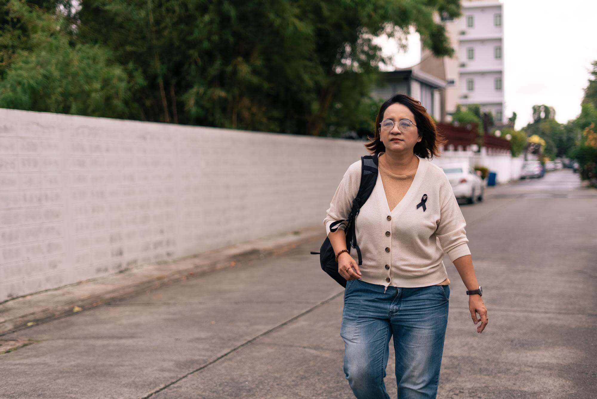 Latina woman in a cardigan walking alone along a quiet street at an easy pace