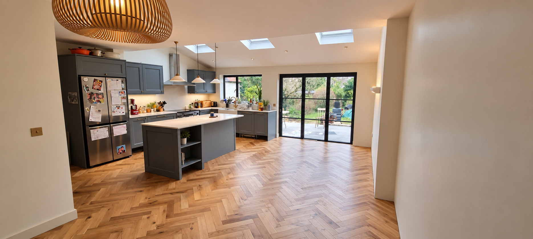 Open-plan kitchen extension with three roof lights, a grey island, herringbone oak floor and black-framed doors to the garden