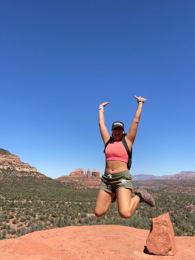 woman in baseball hat jumping for joy in rocky desert