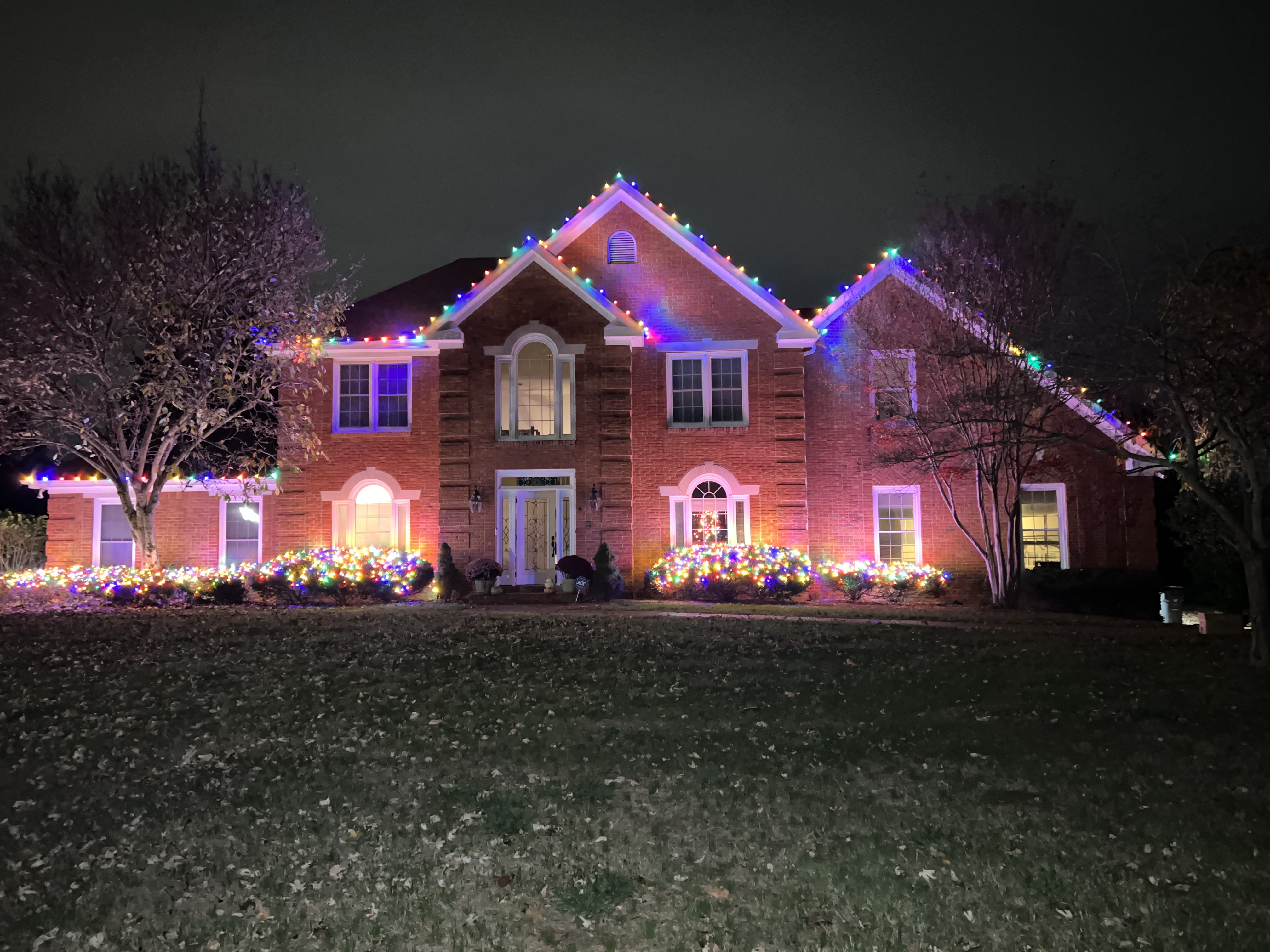 Brick two-story home with multicolor roofline and lit shrubs