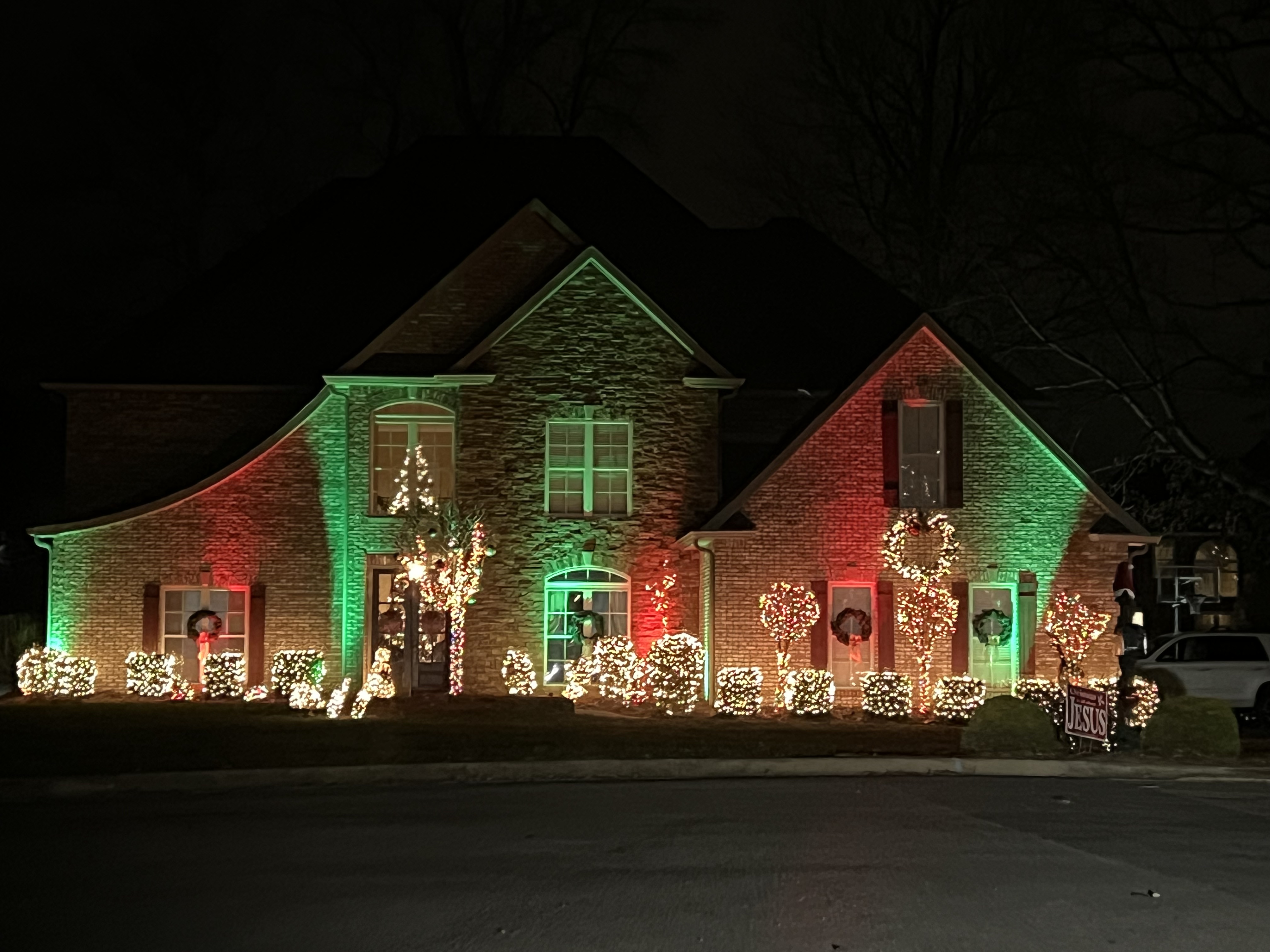 Brick home with red and green wall washes, lit trees and wreaths