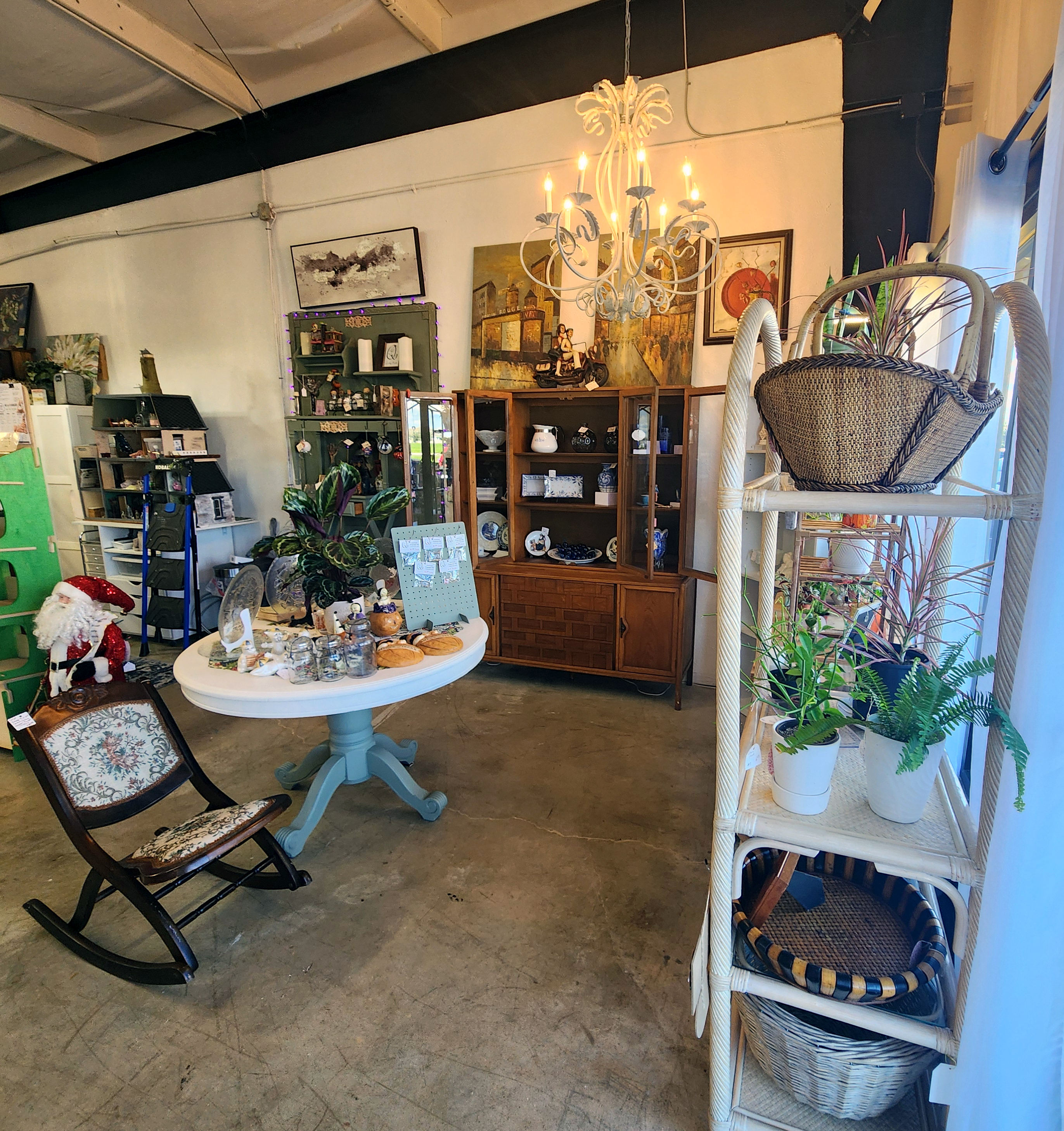 The shop interior with a chandelier, round table, cabinet, potted plants, and wicker shelving