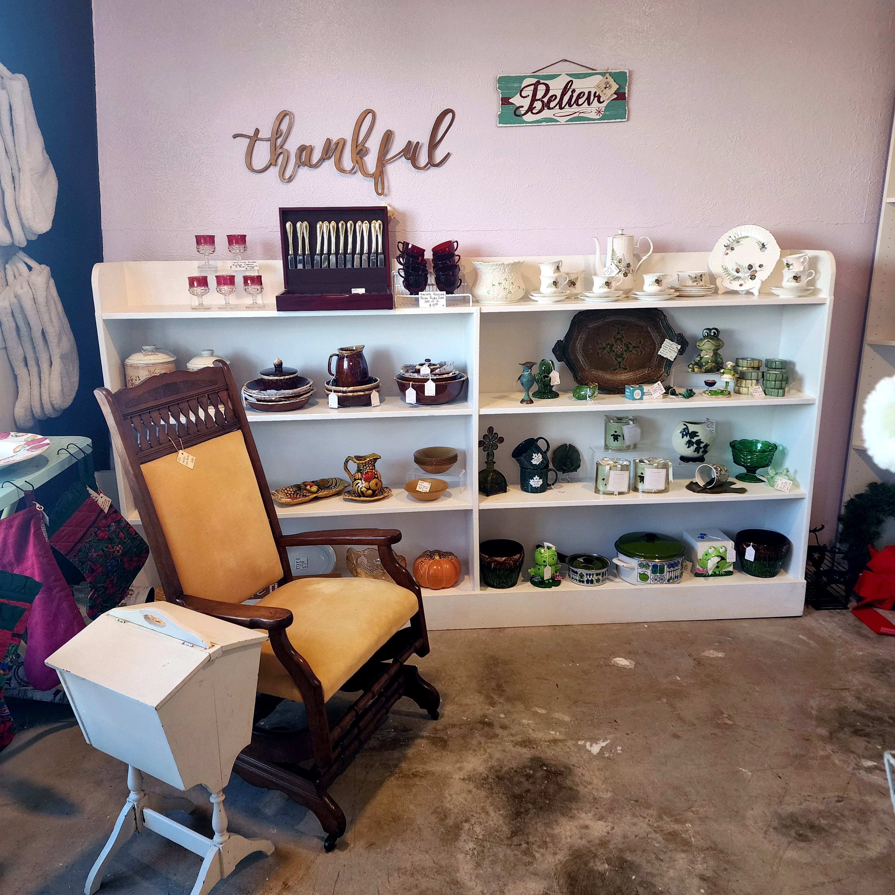 A yellow rocking chair beside white pottery shelves and a 'thankful' wall