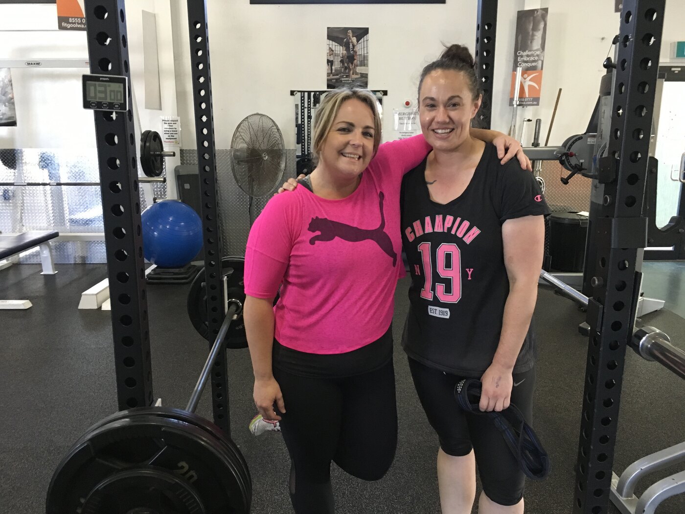 Two people smiling together beside strength-training equipment at the gym.