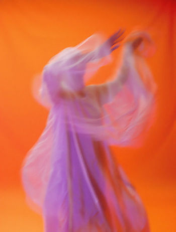 Blurred dancer in lavender fabric against orange Blurred dancer in lavender fabric against orange