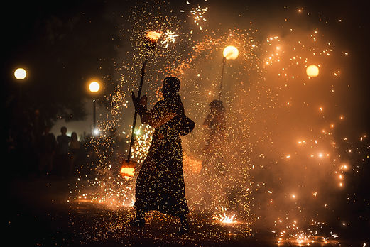 Silhouetted fire performer at night swinging a flaming staff, surrounded by a shower of glowing orange sparks