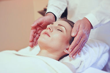 Woman lying peacefully with eyes closed as a practitioner holds his hands gently on either side of her head during an energy healing session Woman lying peacefully with eyes closed as a practitioner holds his hands gently on either side of her head during an energy healing session
