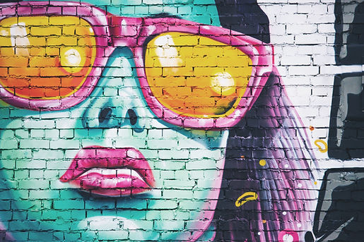 Colorful street art mural on a brick wall of a woman’s face in turquoise with pink sunglasses, glowing yellow lenses and bright pink lips
