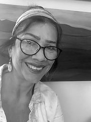 Black-and-white photo of a smiling woman in glasses and a headband in front of a landscape painting Black-and-white photo of a smiling woman in glasses and a headband in front of a landscape painting