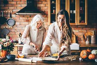 Older woman and her adult daughter baking a pie together in a cozy brick kitchen decorated with pumpkins and flowers Older woman and her adult daughter baking a pie together in a cozy brick kitchen decorated with pumpkins and flowers